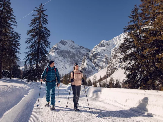 Wanderhotel Tirol: durchs Karwendel wandern und biken Paar beim Schneeschuhwandern auf Bergweg mit schneebedeckten Bergen