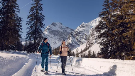 Paar beim Schneeschuhwandern auf Bergweg mit schneebedeckten Bergen