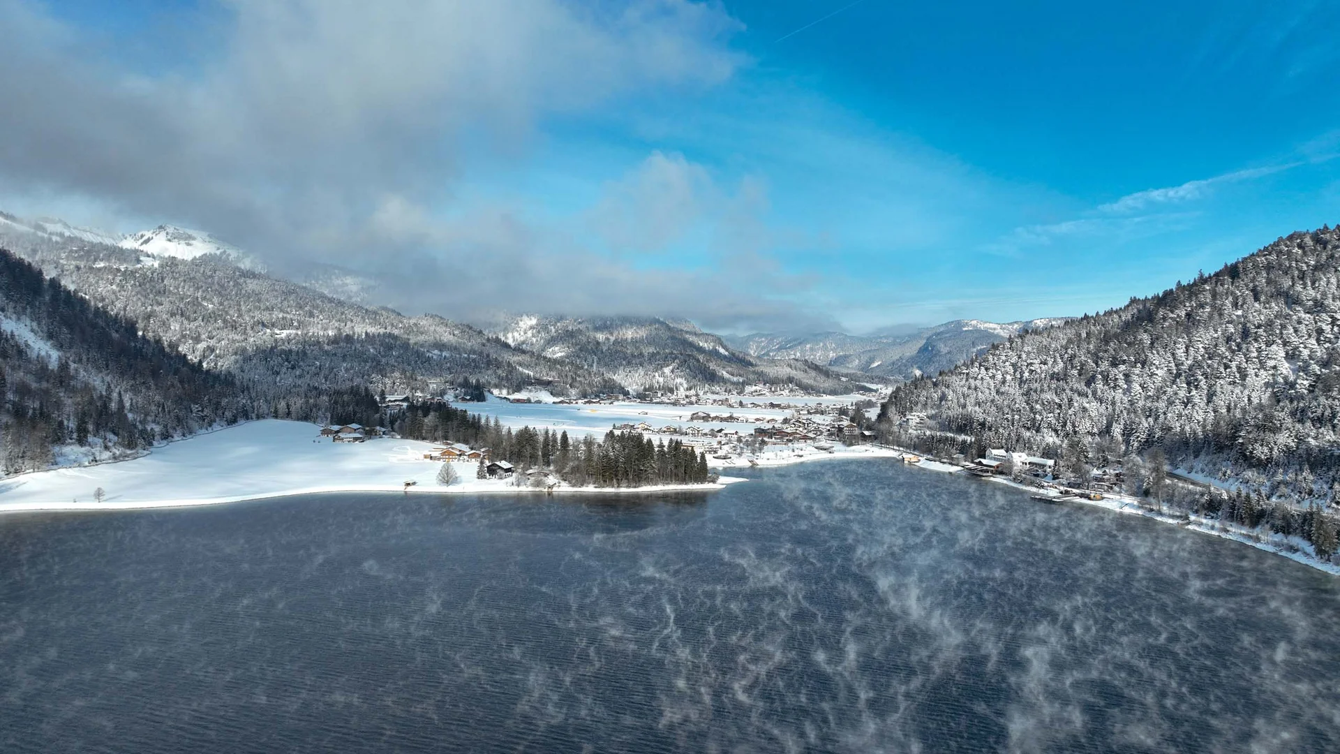 In, auf und rund um den Achensee Winterlandschaft mit schneebedeckten Bergen und einem rauchenden See unter blauem Himmel