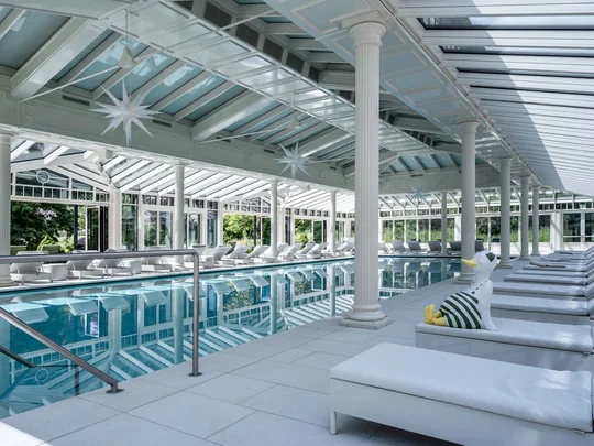 Auf in ein romantisches Hotel in Tirol Hallenbad mit weißen Liegen und Glasdach im sonnendurchfluteten Raum