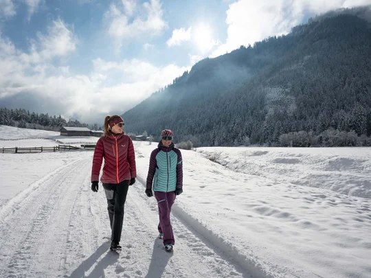 Wanderhotel Tirol: durchs Karwendel wandern und biken Zwei Frauen gehen bei sonnigem Winterwetter auf einem verschneiten Weg in den Bergen spazieren