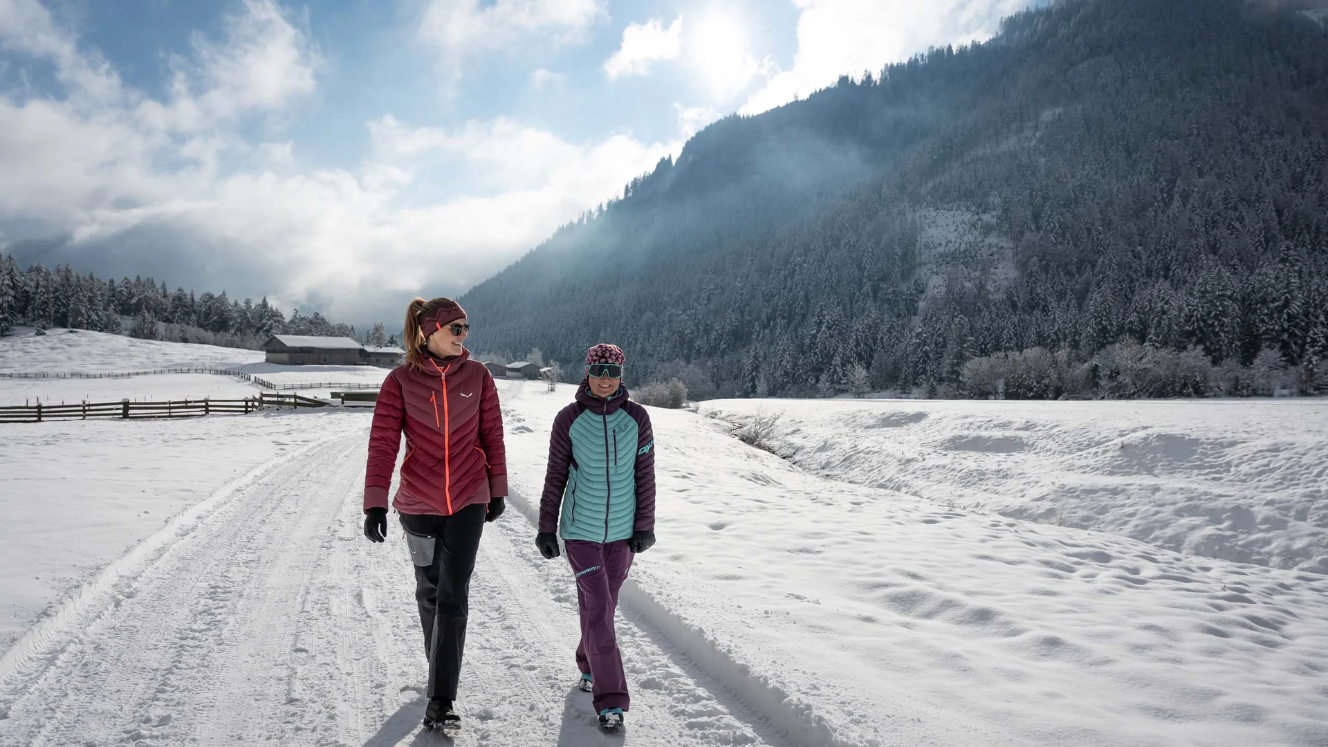 Wanderhotel Tirol: durchs Karwendel wandern und biken Zwei Frauen gehen bei sonnigem Winterwetter auf einem verschneiten Weg in den Bergen spazieren