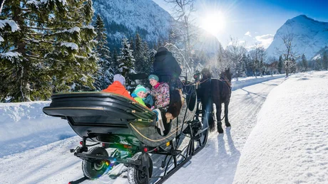 Familie in Pferdeschlitten im Schnee vor verschneiten Bergen