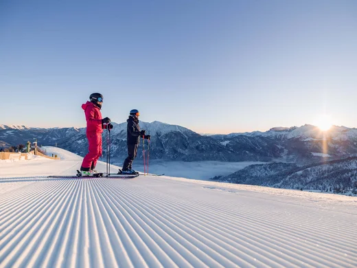 Den Achensee entdecken Zwei Skifahrer stehen auf einer präparierten Piste mit Blick auf schneebedeckte Berge bei Sonnenaufgang