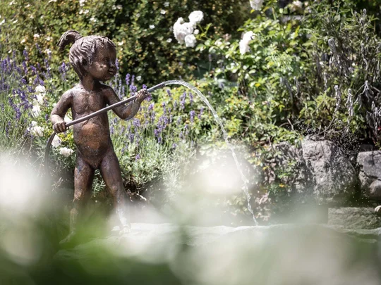 Der Wiesenhof in Pertisau und die Familie Entner mit Team Bronzefigur eines Kindes mit Wasserstrahl in einem Garten mit Blumen