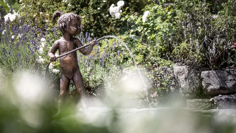 Bronzefigur eines Kindes mit Wasserstrahl in einem Garten mit Blumen