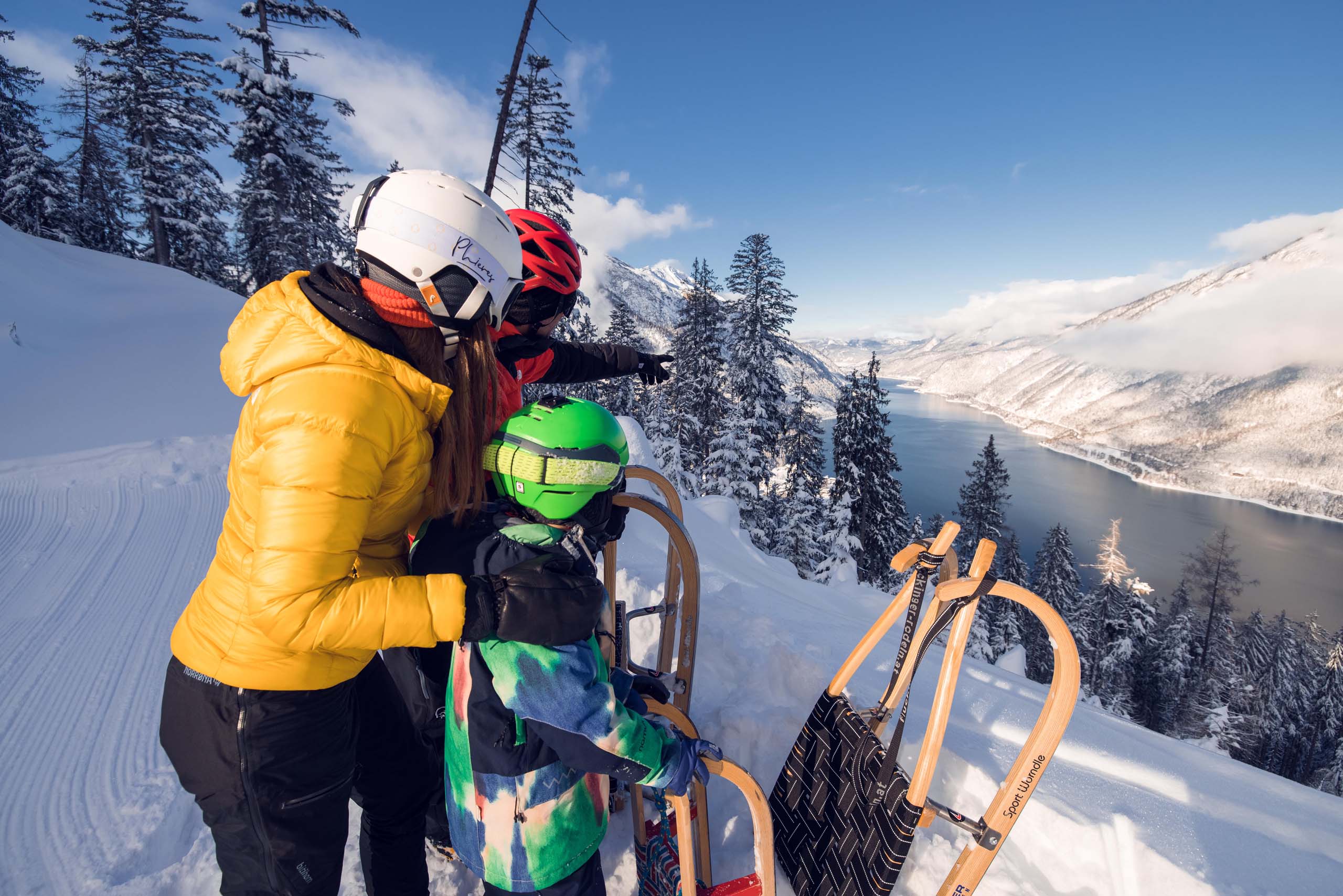 Euer Familienhotel am Achensee Familie mit Schlitten auf verschneitem Berg mit Blick auf Fluss und bewaldete Täler