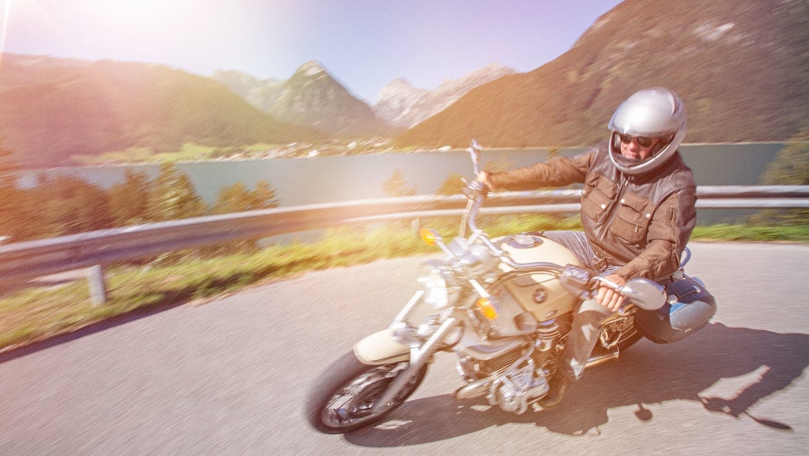 Motorradfahrer fährt an einem malerischen See entlang.