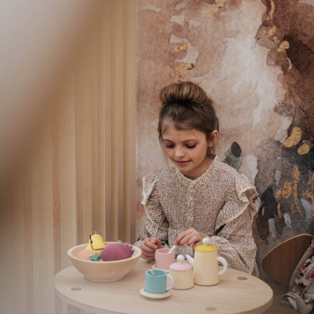 Mädchen spielt mit Spielzeugtassen und -motiven.