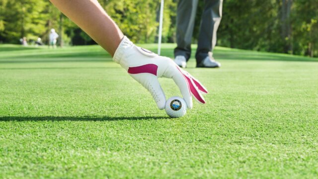 Golfspieler hebt einen Ball auf dem Grün.