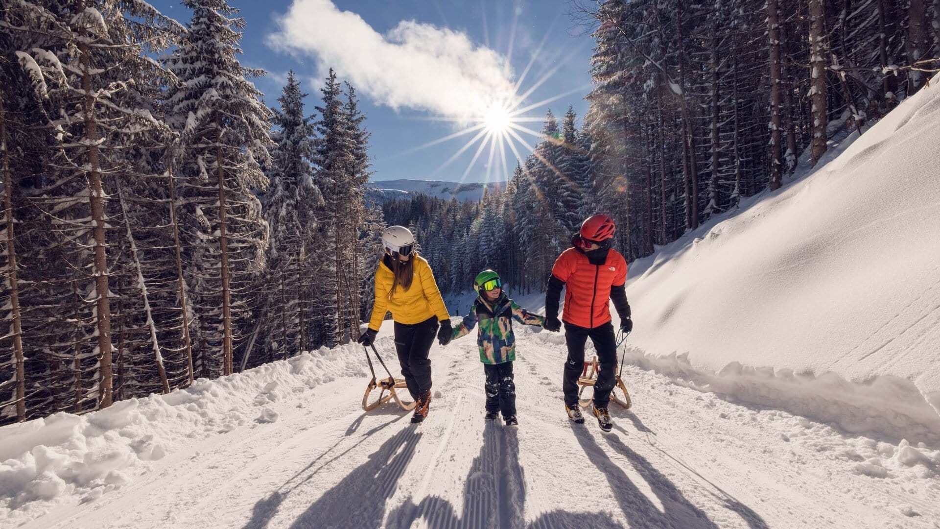 Familie beim Rodeln im verschneiten Wald.